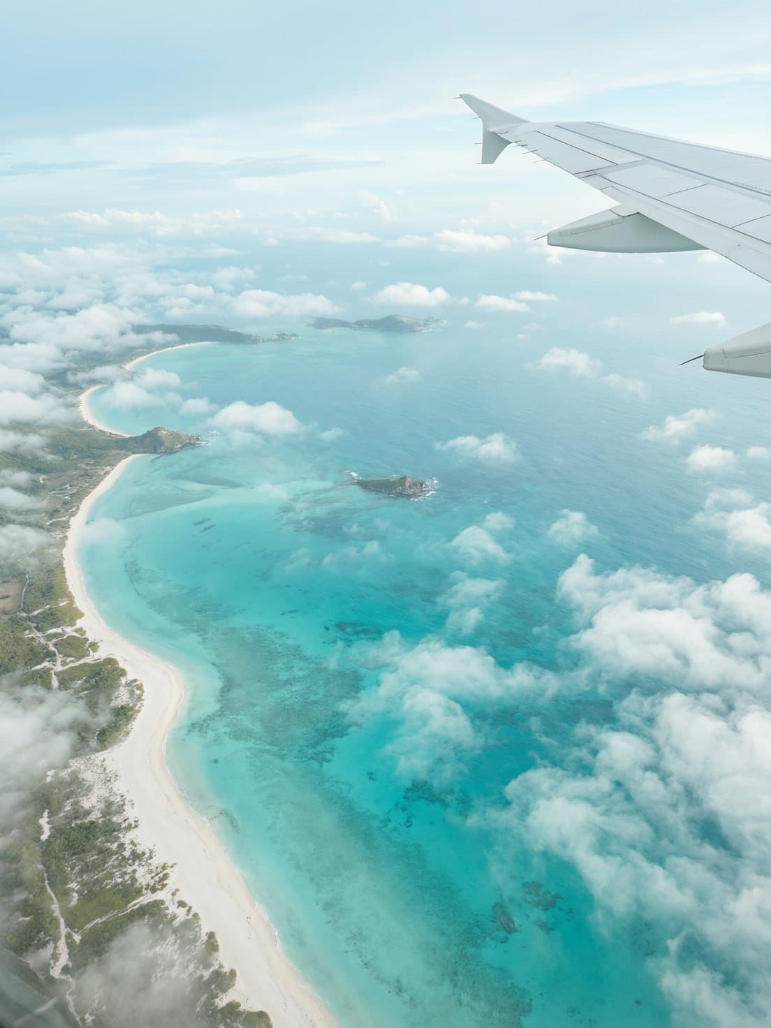 Vista da janela do avião: praia de água azul-turquesa entre nuvens